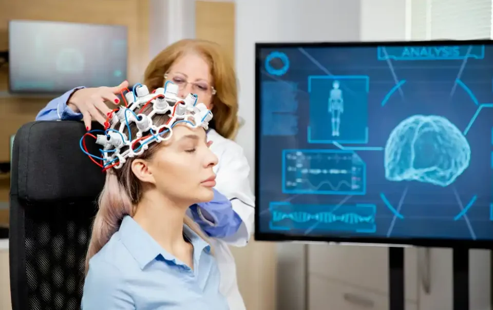 Neuroscientist performing brain scan using neuroplasticity monitoring equipment on a calm female patient, with brain activity data on digital screen - Save your Brain Wellness