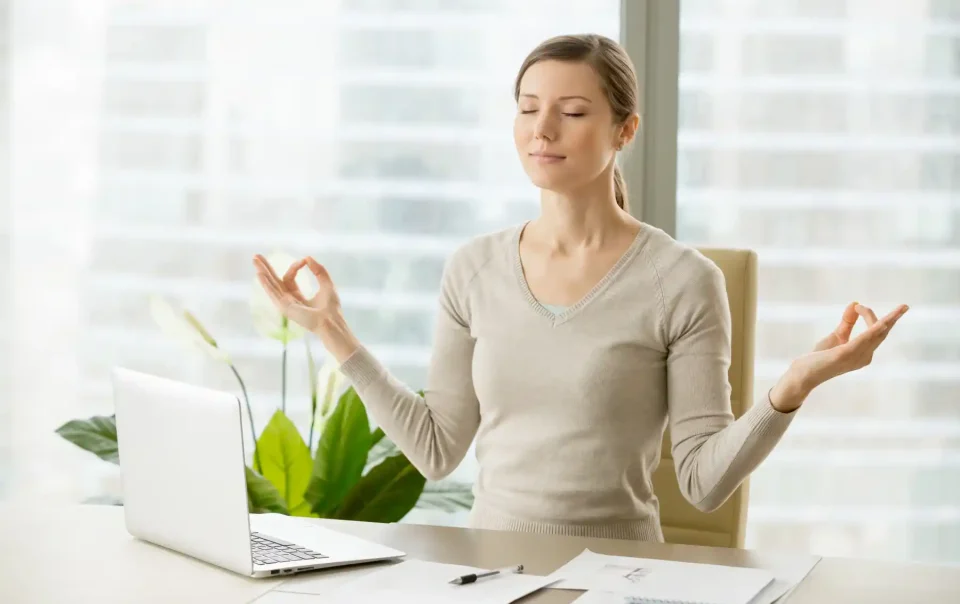 Woman practicing mindfulness meditation at her desk, showing how daily habits like meditation can support brain growth and mental wellness. Save your Brain Wellness