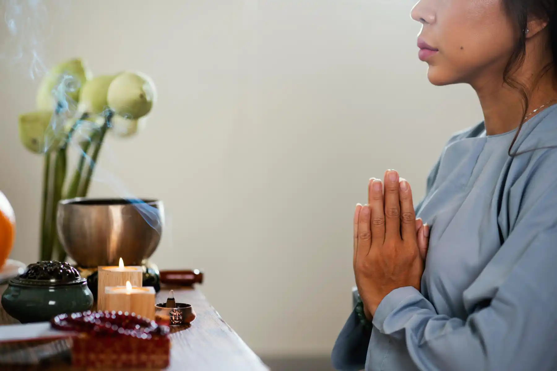 A woman meditating in prayer position beside candles and incense, symbolizing mindfulness and brain wellness