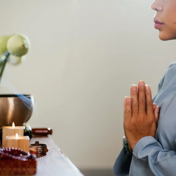A woman meditating in prayer position beside candles and incense, symbolizing mindfulness and brain wellness