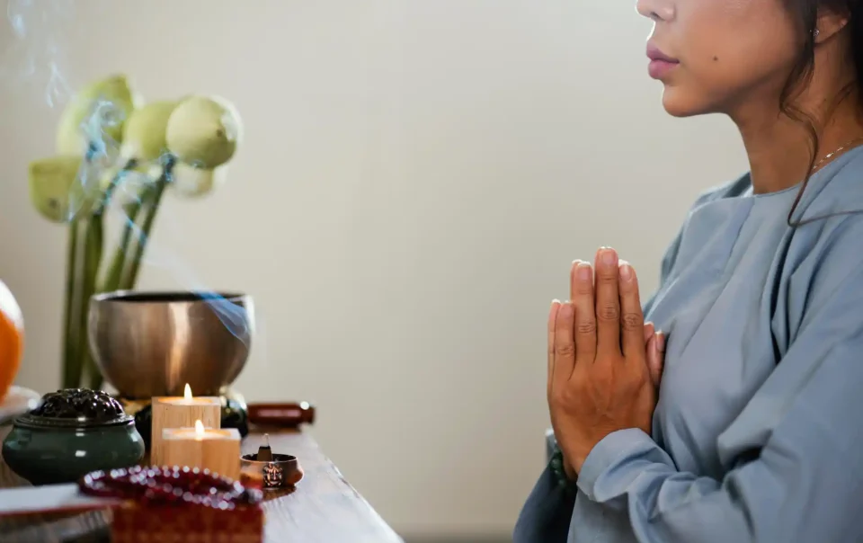 A woman meditating in prayer position beside candles and incense, symbolizing mindfulness and brain wellness