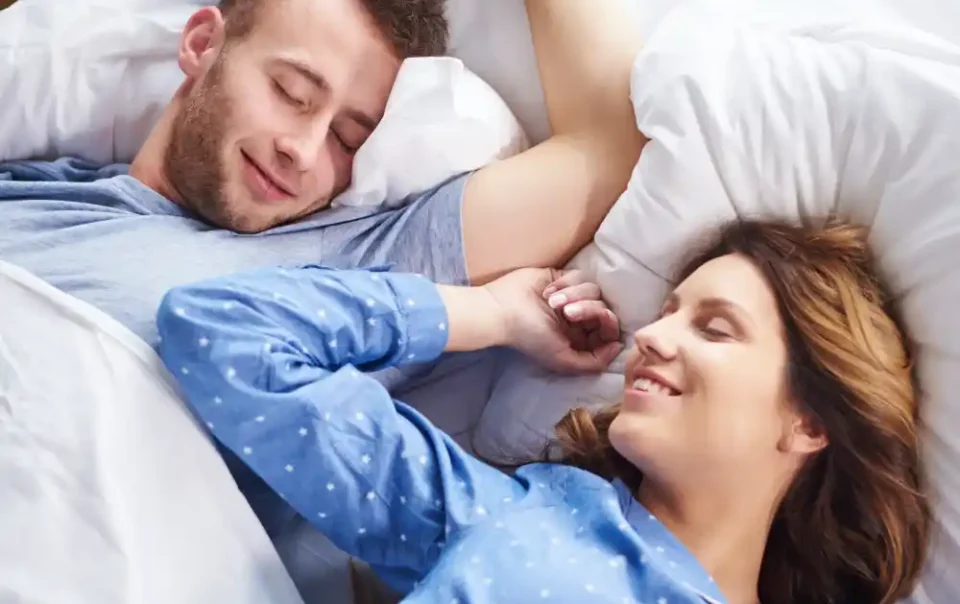 Happy couple sleeping peacefully in bed after successfully completing a sleep restriction therapy program to reset their circadian rhythm