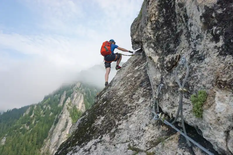 Man climbing steep rocky mountain using safety ropes, symbolizing overcoming mental challenges and unlocking brain motivation.