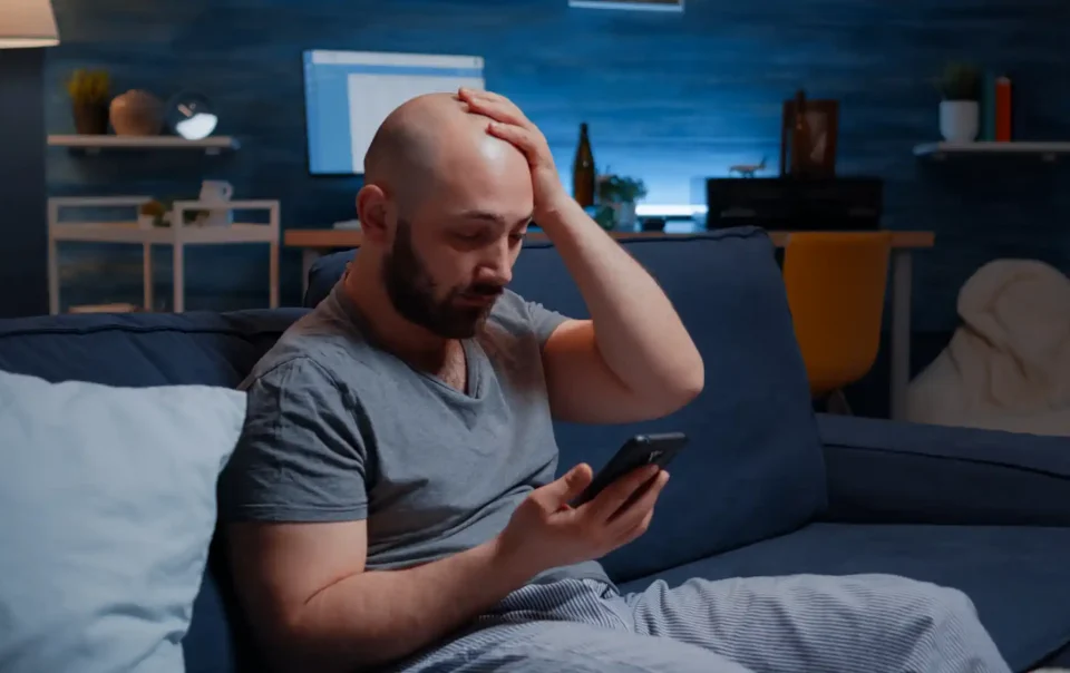 Stressed man overwhelmed by digital addiction and dopamine overload while using smartphone at night