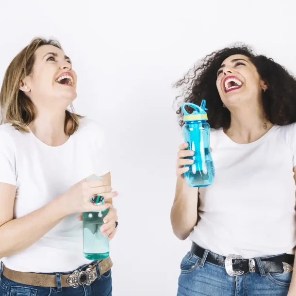 Two happy women holding water bottles, laughing and enjoying hydration for better brain health and focus.