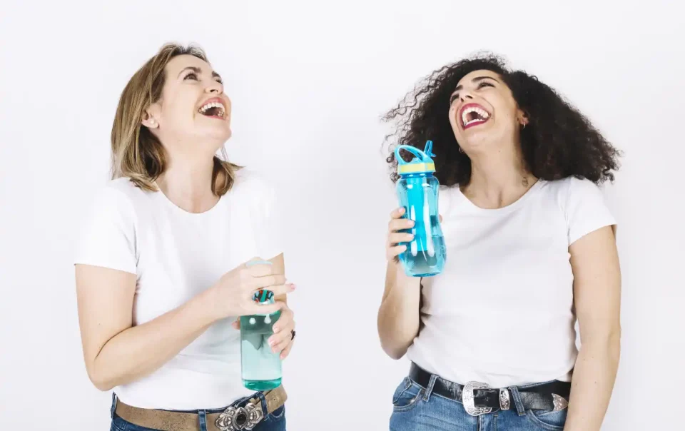Two happy women holding water bottles, laughing and enjoying hydration for better brain health and focus.