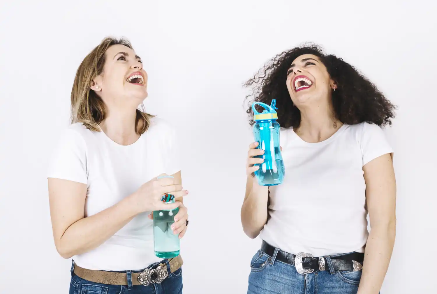 Two happy women holding water bottles, laughing and enjoying hydration for better brain health and focus. 